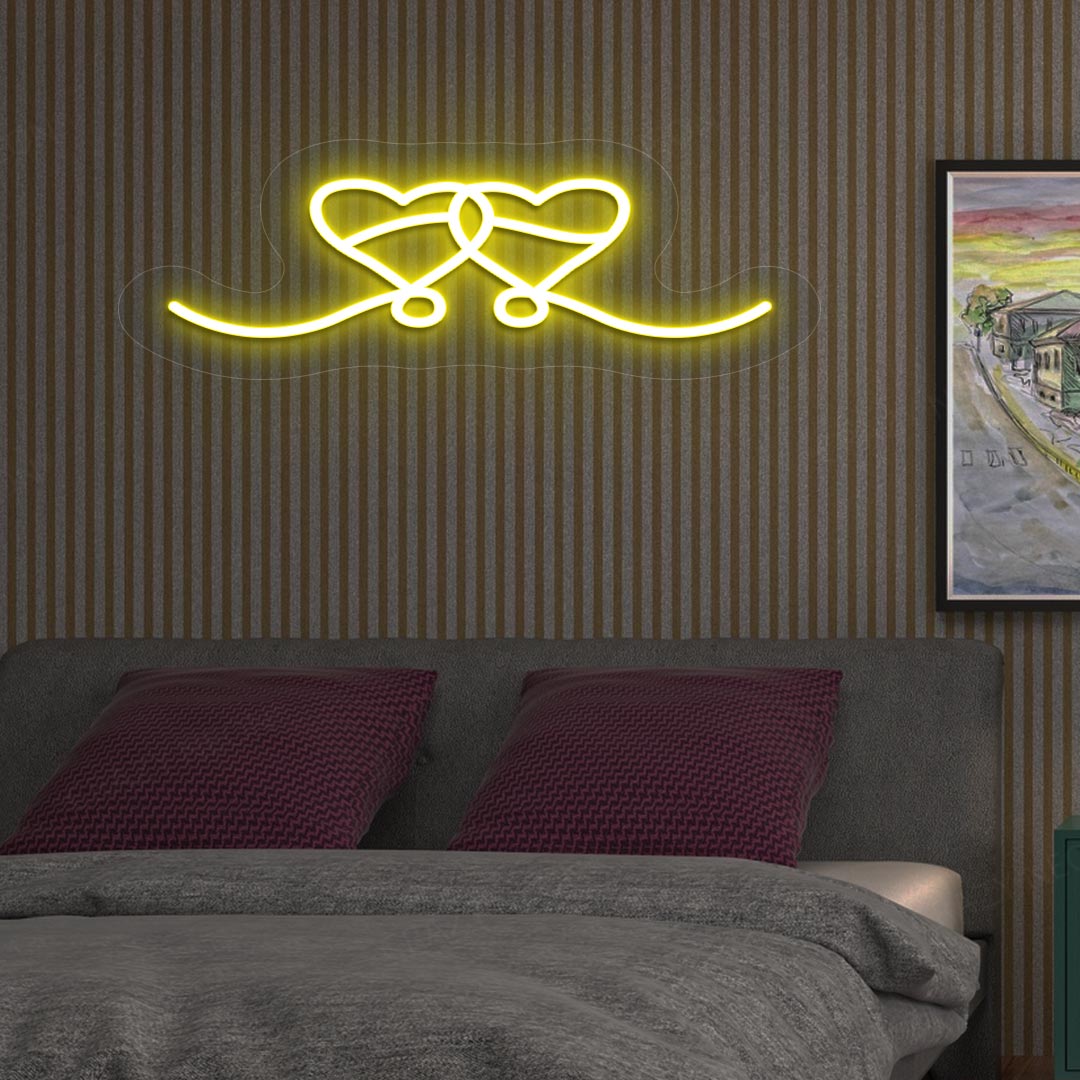 An image depicting a neon sign in the shape of two hearts, illuminated in yellow, on the bedroom wall.