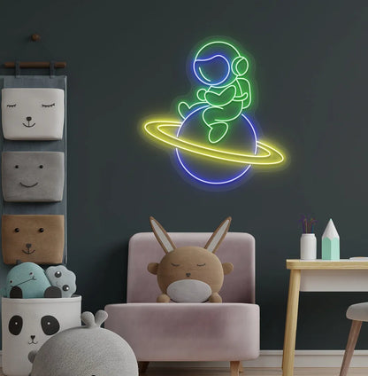 Green astronaut sitting on planet LED neon sign for space-themed bedroom.