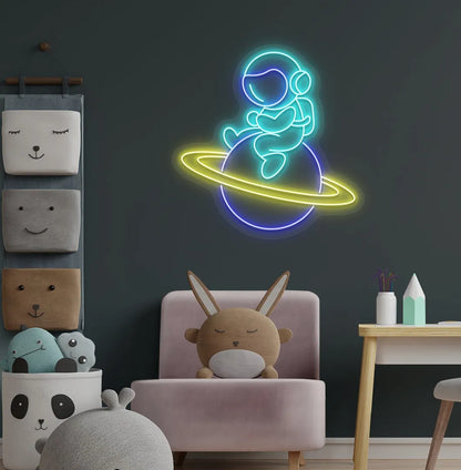 Stylish astronaut sitting on planet neon sign mounted on children's wall in ice blue color.