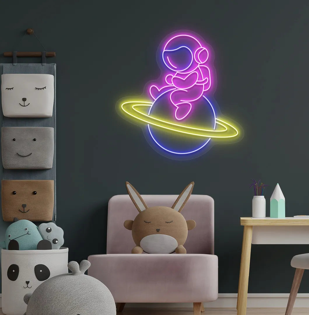 Stylish astronaut sitting on planet neon sign mounted on children's wall in pink color.