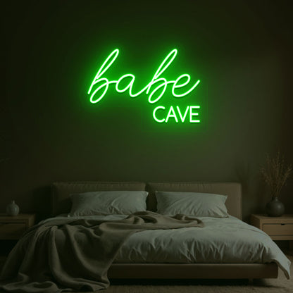 Image of a babe cave neon sign glowing on a bedroom wall in green color.