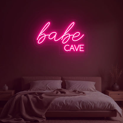 Image of a babe cave neon sign glowing on a bedroom wall in pink color.