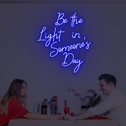 A soft blue LED "Be the light in someone's day" neon sign is glowing on the wall.