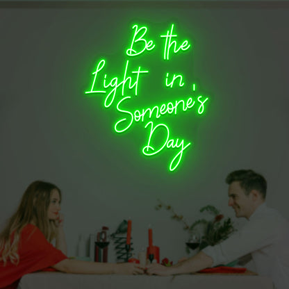 Image of an inspirational LED neon sign, "Be the light in someone's day," mounted on a wall in green color.