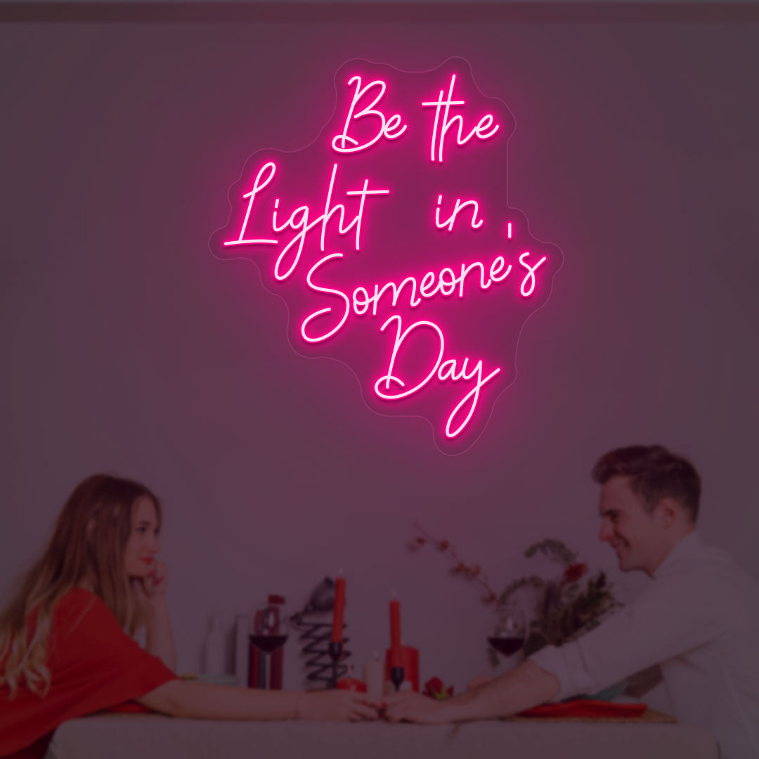 A soft pink LED "Be the light in someone's day" neon sign is glowing on the wall.
