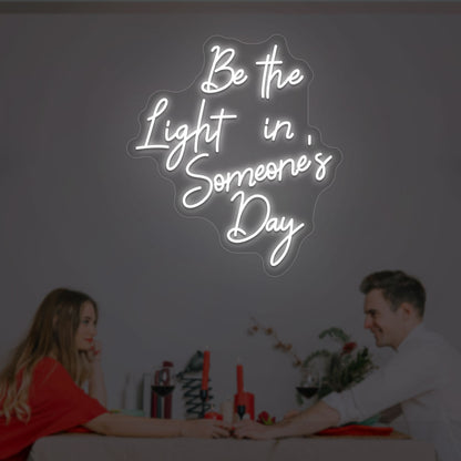 Image of an inspirational LED neon sign, "Be the light in someone's day," mounted on a wall in white color.
