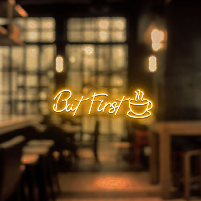 Image of a "but first" neon sign with a cup icon on a cafe entrance door in orange color.