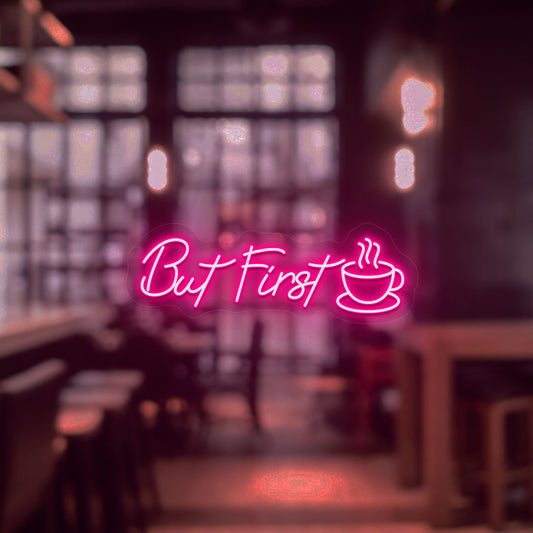 Image of a "but first" neon sign with a cup icon on a cafe entrance door in pink color.
