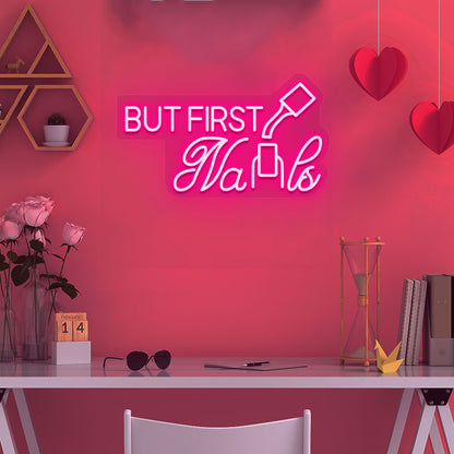 Image of a "but first nails" LED neon sign mounted on a salon wall in pink color.