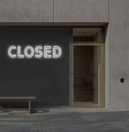Image of a closed bold neon sign glowing on a shop exterior wall in white.