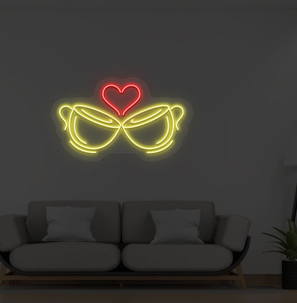 A cup heart LED neon sign in yellow color with two cups and a heart design mounted on a wall.
