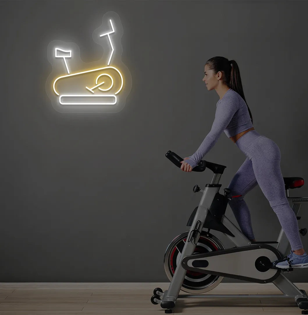 Trendy exercise cycle neon sign in orange mounted on fitness wall.