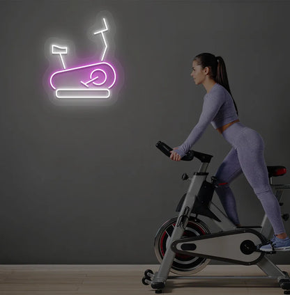 Image of a stylish "exercise cycle" neon sign mounted on gym wall in pink color.