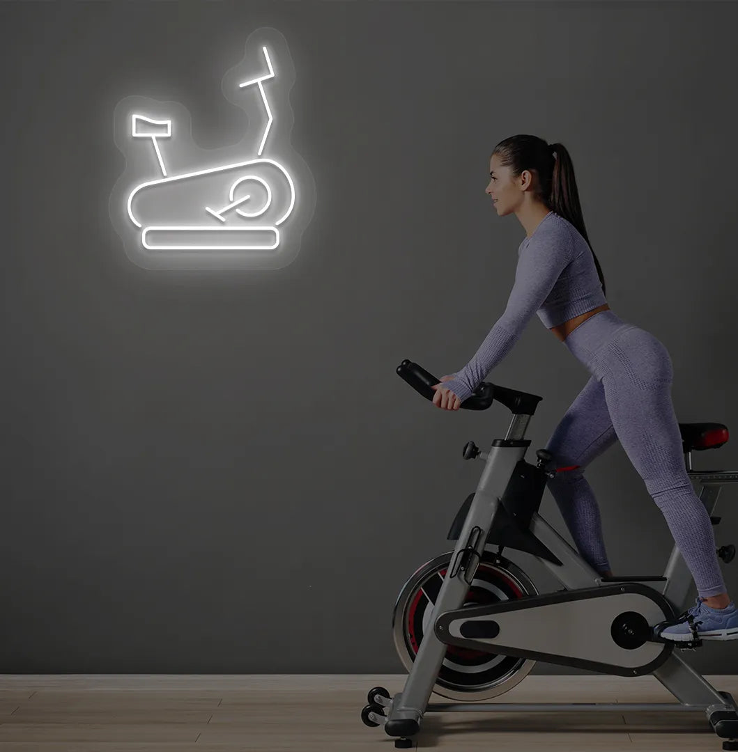 Image of a stylish "exercise cycle" neon sign mounted on gym wall in white color.