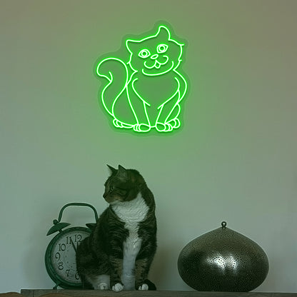 Image of a cat LED neon sign hanging on a wall in green color above a cute cat.