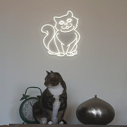 Image of a cat LED neon sign hanging on a wall in warm white color above a cute cat.