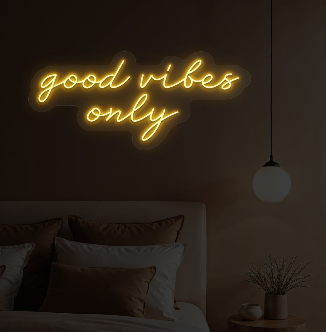 An orange LED "good vibes only" neon sign on a bedroom wall with soft lighting.