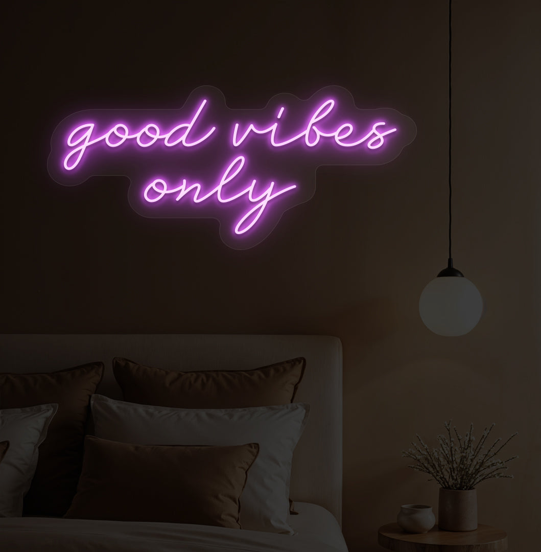 Image of a "Good vibes only" purple neon sign hanging on a bedroom wall. 