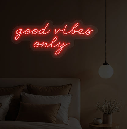 A red LED "good vibes only" neon sign on a bedroom wall with soft lighting.