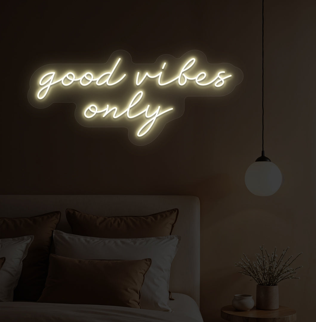 A warm white LED "good vibes only" neon sign on a bedroom wall with soft lighting.