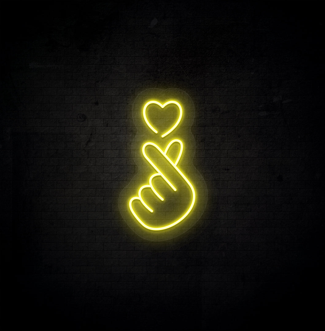 A stylish yellow LED hand heart neon sign glowing on a dark background wall.