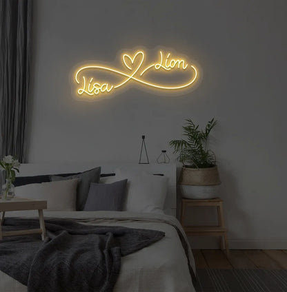 Personalized infinity couple name neon sign mounted on modern bedroom wall in orange color.