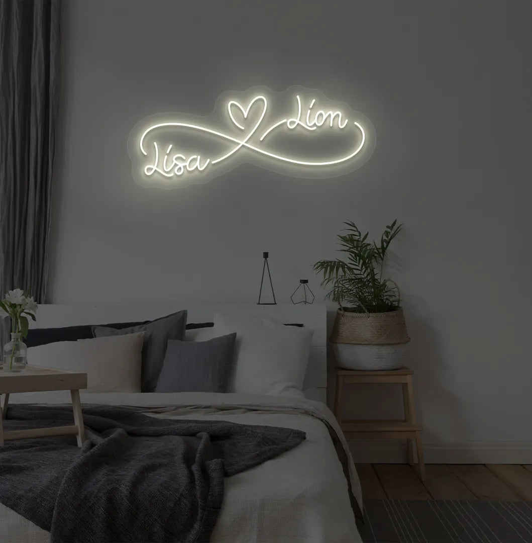 Personalized infinity couple name neon sign mounted on modern bedroom wall in warm white color.