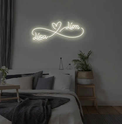 Personalized infinity couple name neon sign mounted on modern bedroom wall in warm white color.