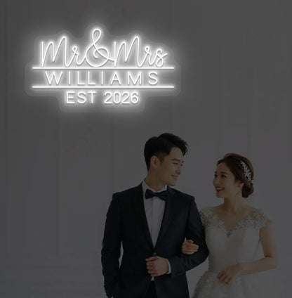Personalized Mr and Mrs wedding neon sign glowing white on wedding backdrop.