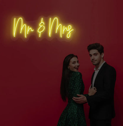 Elegant Mr and Mrs wedding neon sign glowing yellow on wedding backdrop.