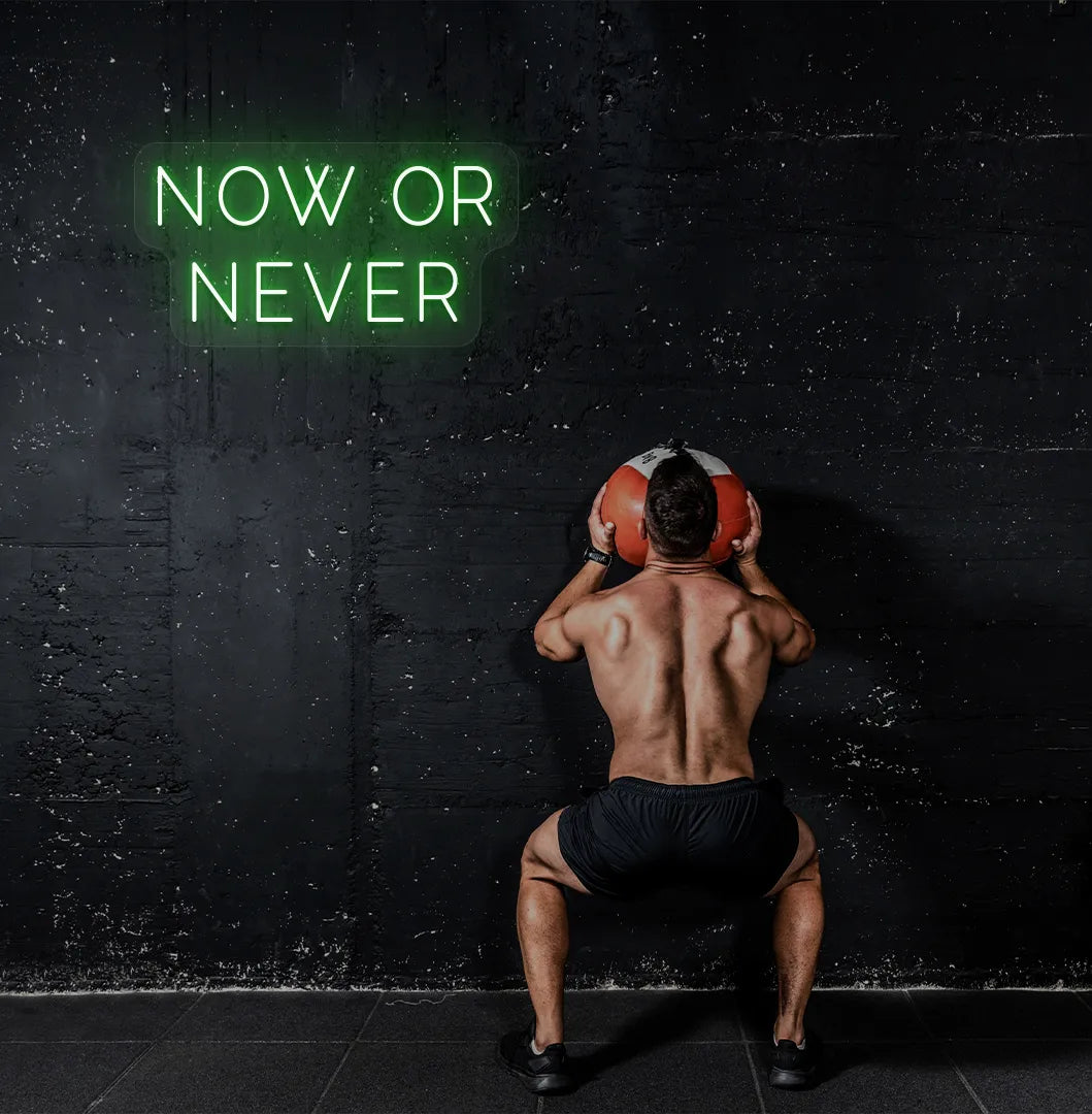 Trendy "now or never" neon sign in green mounted on fitness wall.