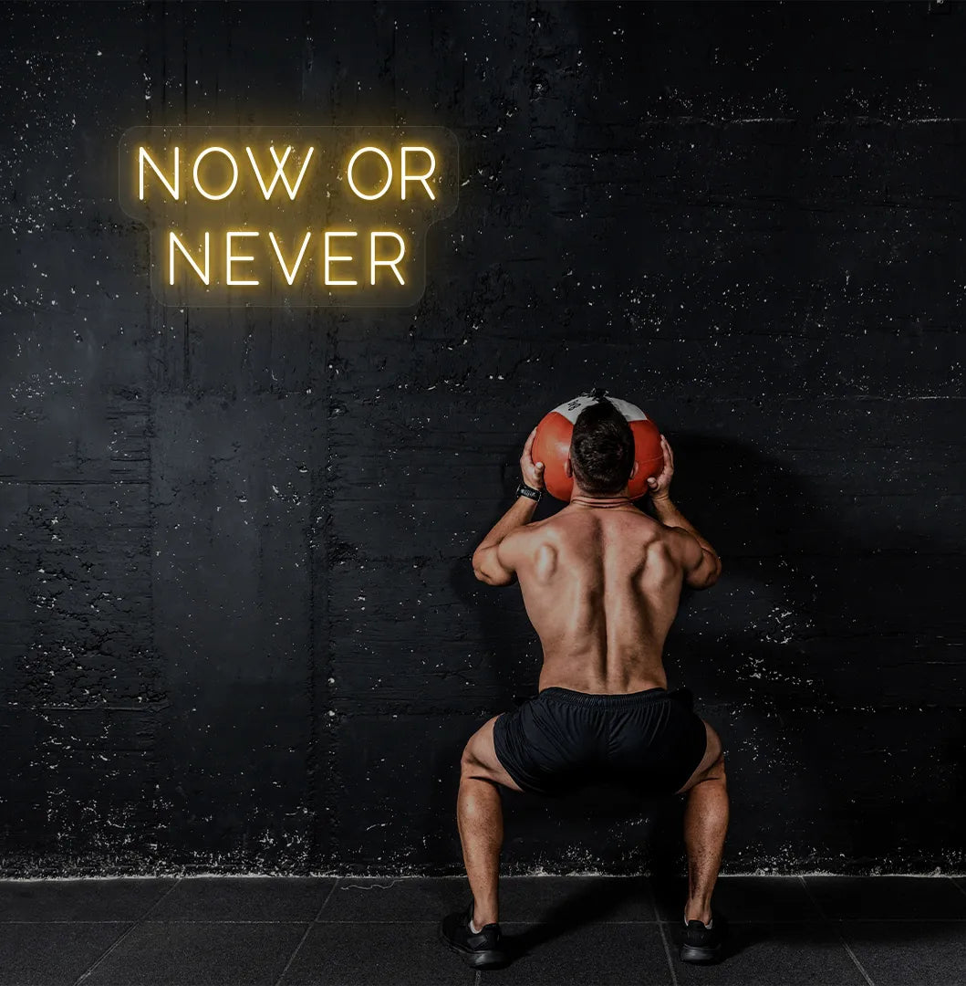 Trendy "now or never" neon sign in orange mounted on fitness wall.