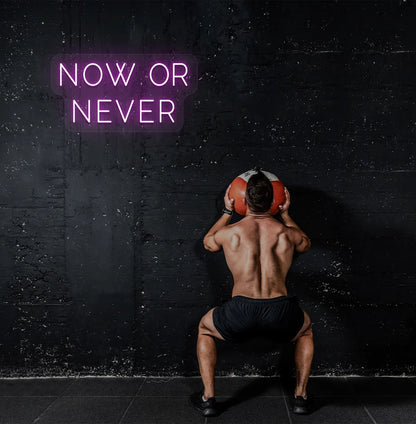 Trendy "now or never" neon sign in purple mounted on fitness wall.