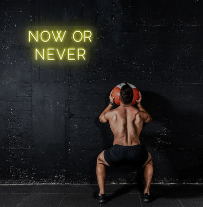 Trendy "now or never" neon sign in yellow mounted on fitness wall.