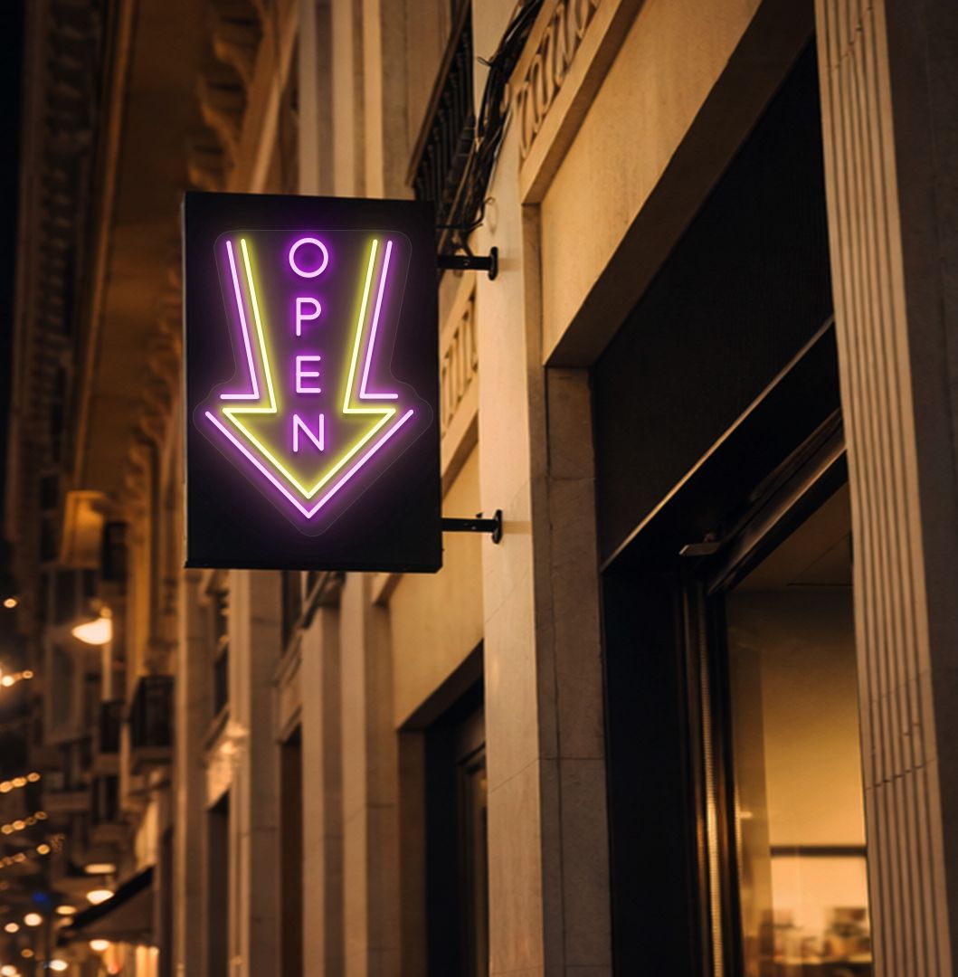 Directional open arrow neon sign glowing pink on outdoor stand.