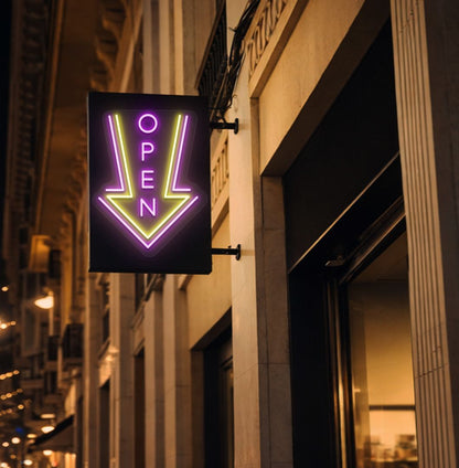 Directional open arrow neon sign glowing pink on outdoor stand.