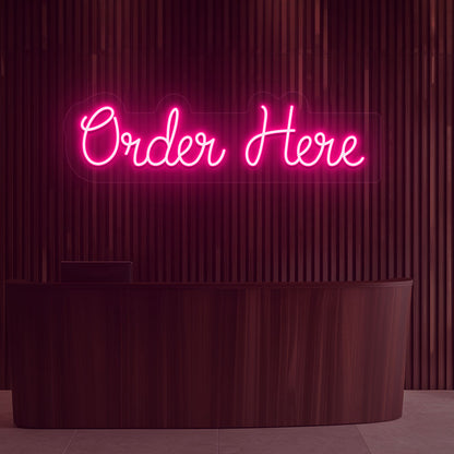 Image of a neon sign that says "order now" glowing in pink color on a wooden wall above the counter in a cafe.