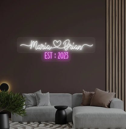 Romantic custom Couple Name EST neon sign glowing white on aesthetic wall.