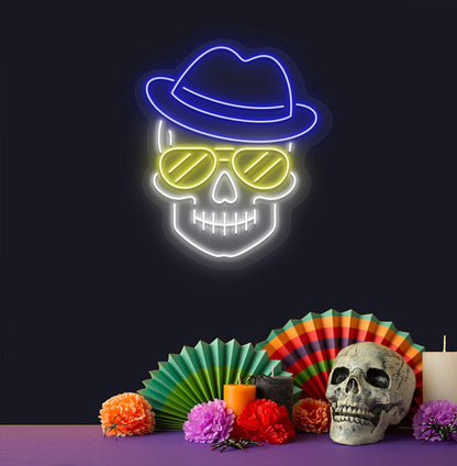 Image of a skull with hat and sunglasses neon sign above human skull glowing on wall in blue color.