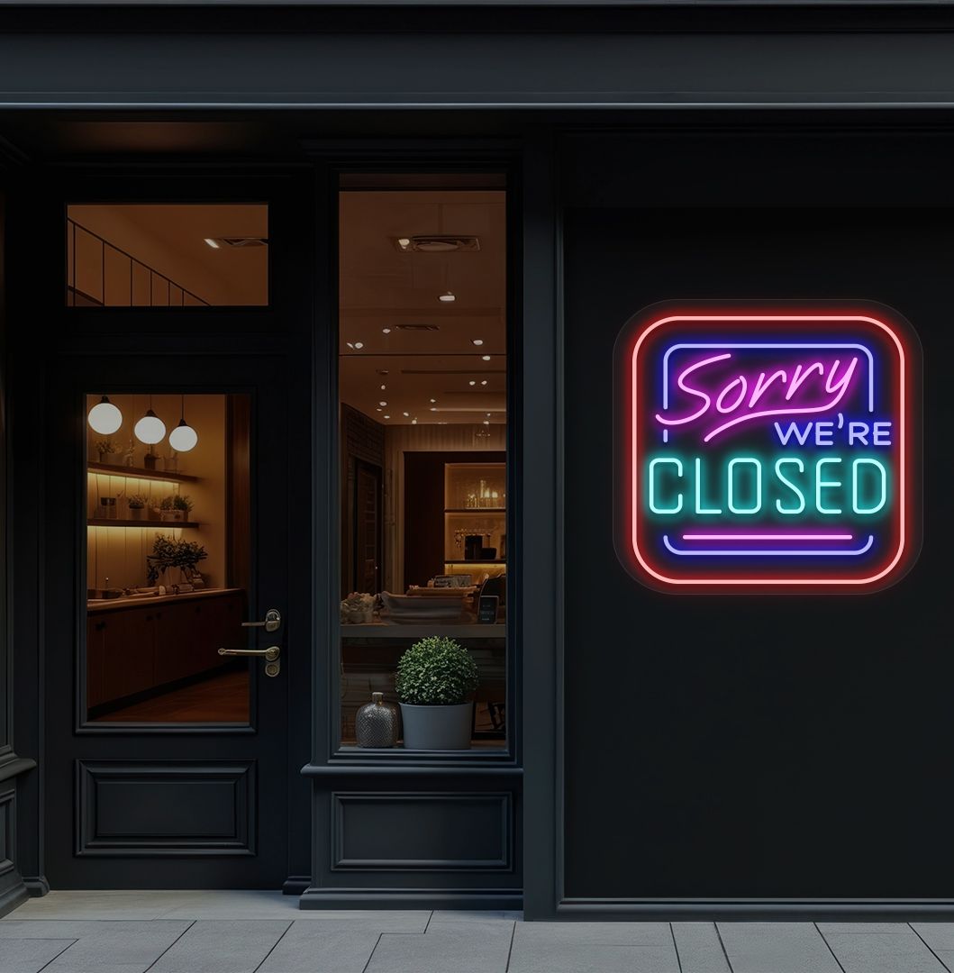 Image of a "Sorry, We're Closed" neon sign glowing on a shop exterior wall in ice blue color.