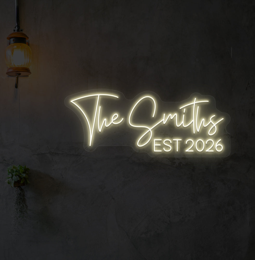 Custom name LED neon sign "The Smiths" glowing warm white on wall.