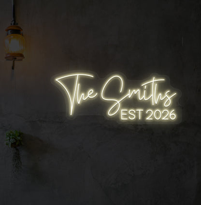 Custom name LED neon sign "The Smiths" glowing warm white on wall.