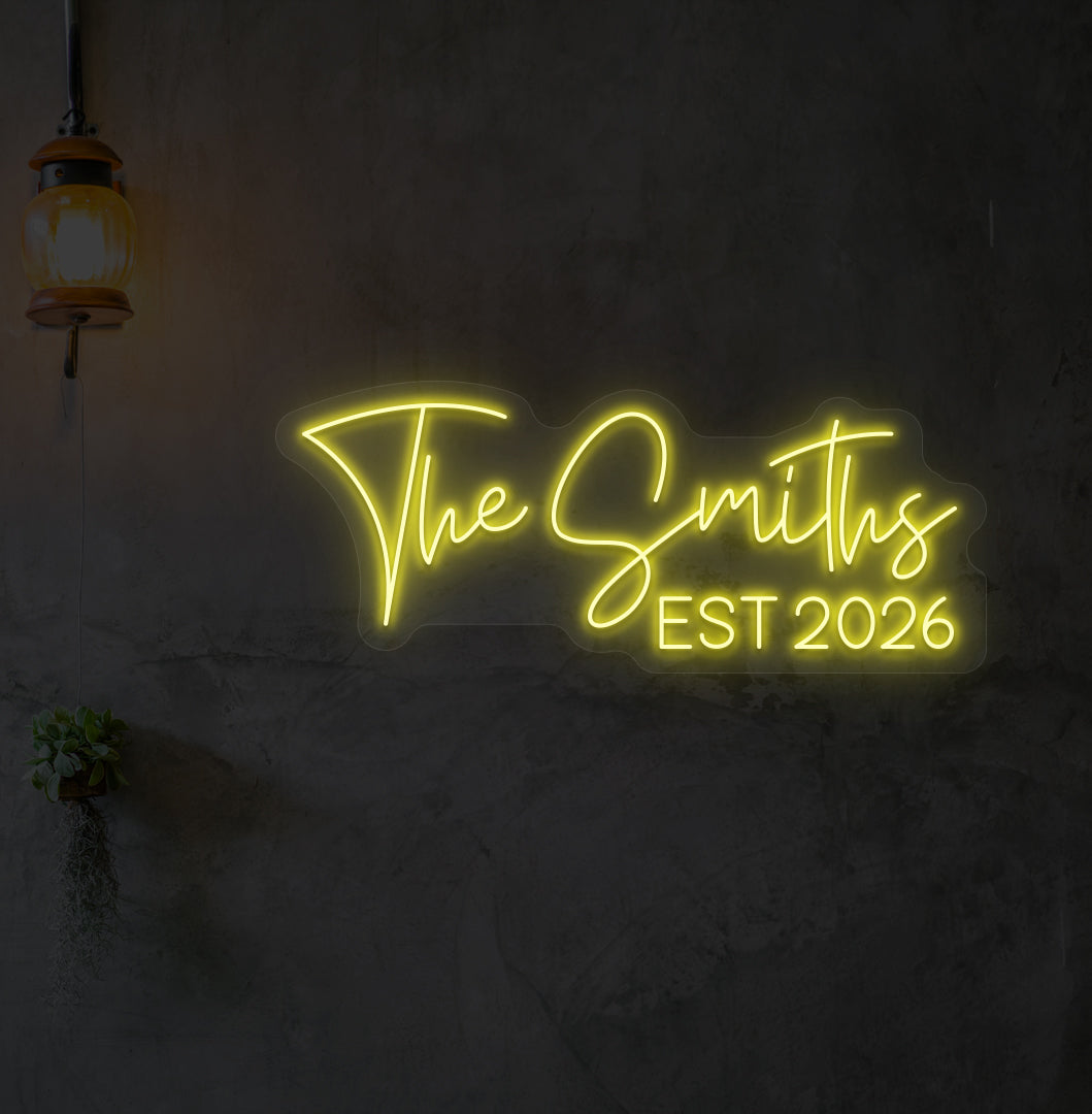 Custom name LED neon sign "The Smiths" glowing yellow on wall.