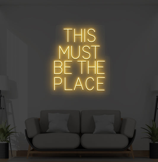 Image of a "this must be the place" neon sign glowing on a living room wall in orange color.