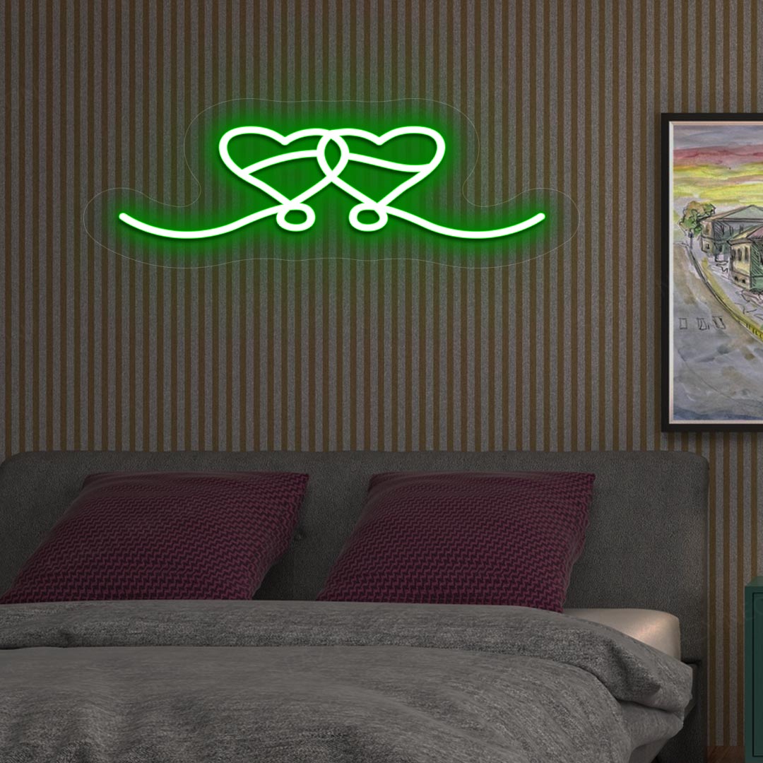 A green LED two-hearts neon sign glowing on a romantic bedroom wall.