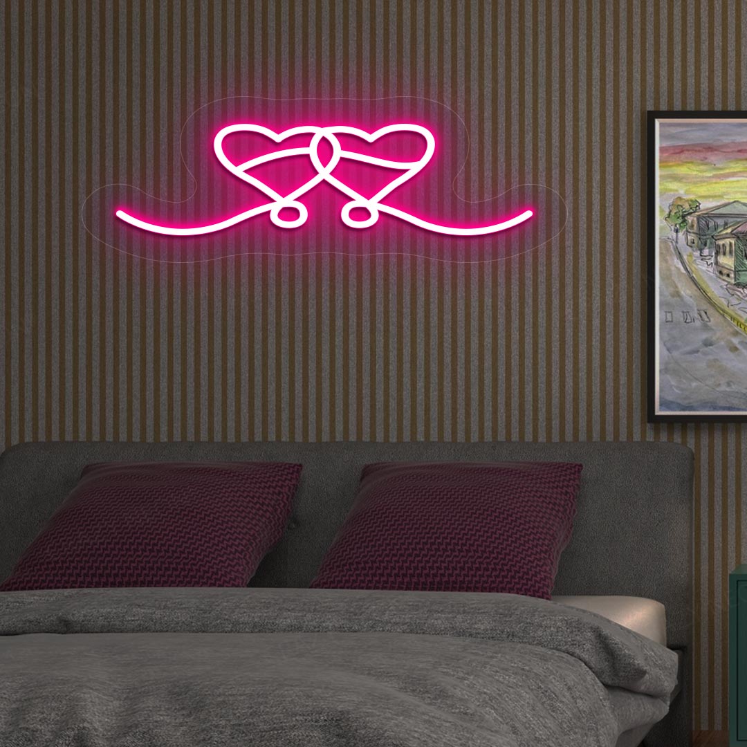 An image depicting a neon sign in the shape of two hearts, illuminated in pink, on the bedroom wall.
