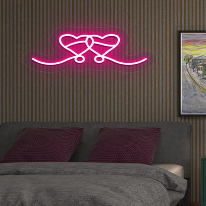 An image depicting a neon sign in the shape of two hearts, illuminated in pink, on the bedroom wall.
