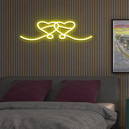 An image depicting a neon sign in the shape of two hearts, illuminated in yellow, on the bedroom wall.
