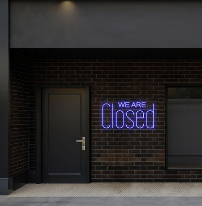 Image of a we are closed LED neon sign glowing on shop exterior wall in blue color.