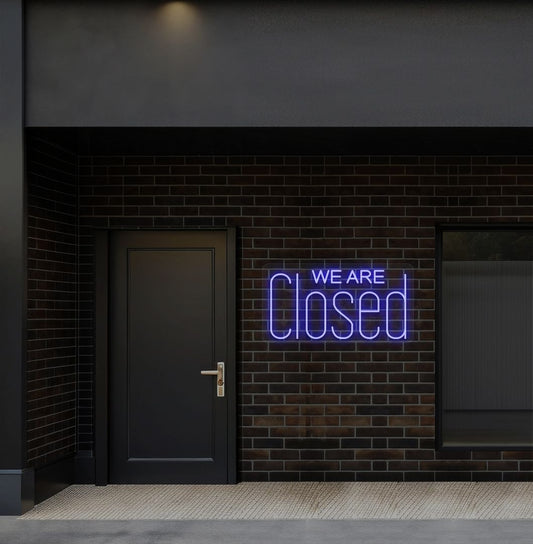 Image of a we are closed LED neon sign glowing on shop exterior wall in blue color.